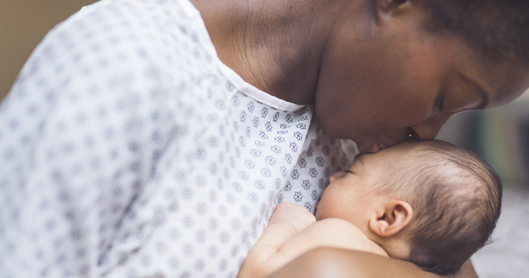 African American mother in a hospital gown kissing newborn