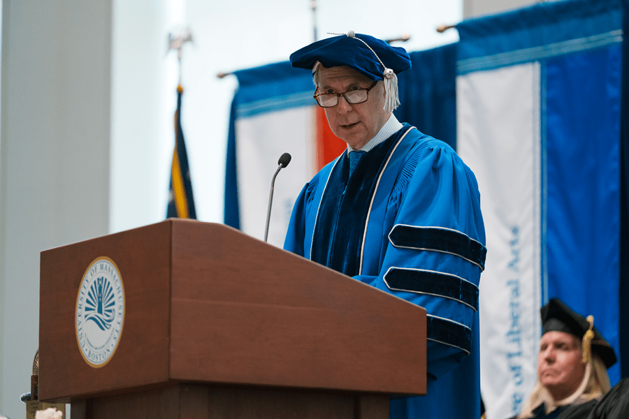 The Honorable David Lowy, in blue academic regalia, standing at a podium.