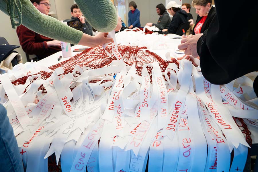 Students helping tie white ribbon on Hanska Luger art piece