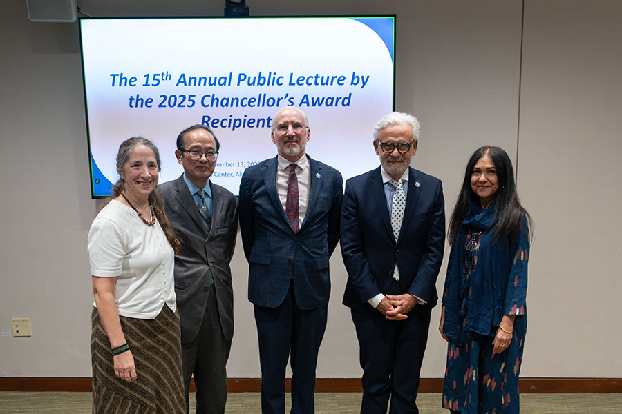 Distinguished faculty and staff from UMass Boston stand in front of a screen reading, 